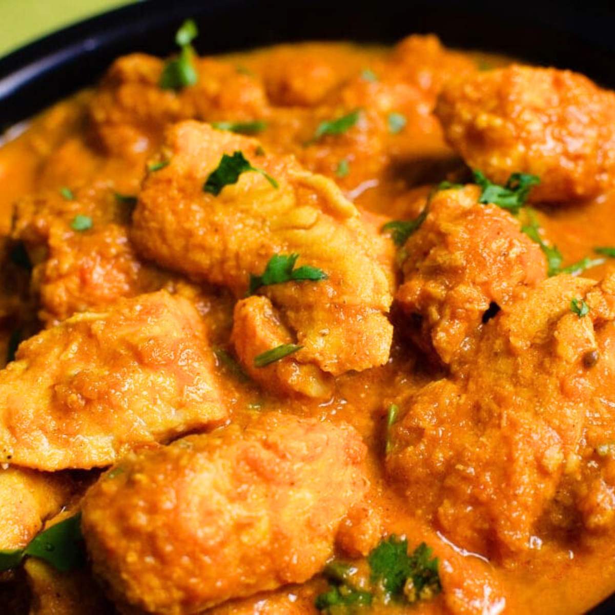 a close-up of a bowl of fish curry The dish is a vibrant orange color and is filled with chunks of fish, tomatoes, and a creamy sauce.