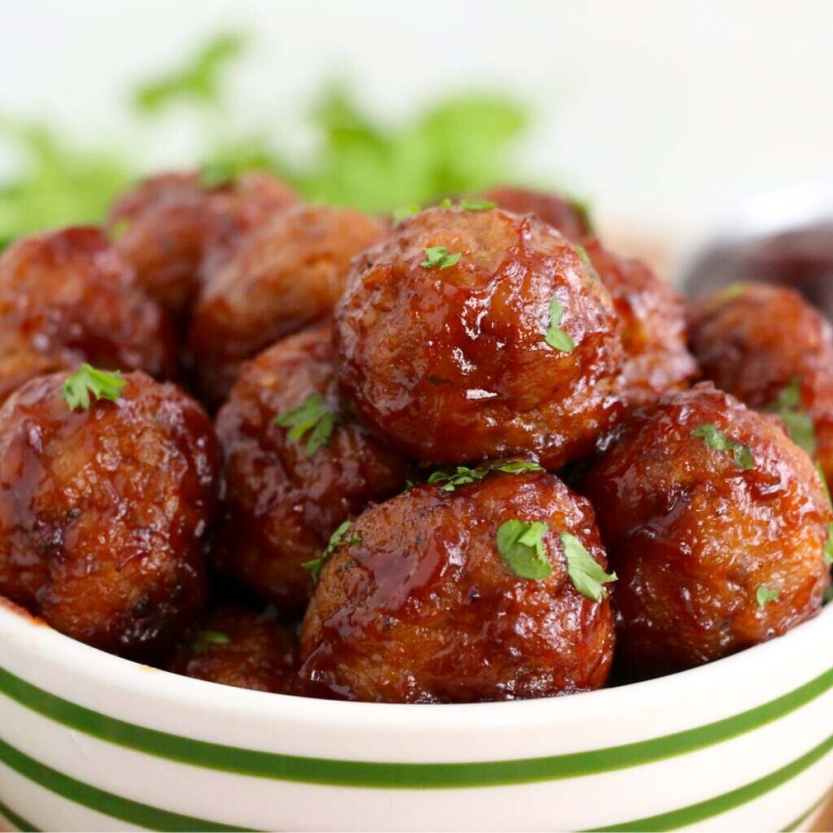 A bowl of sweet and sour meatballs coated in a tangy sauce, garnished with fresh parsley.