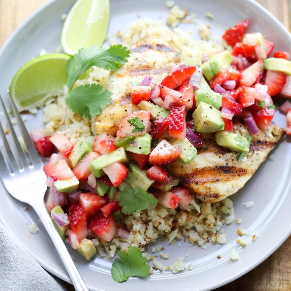 Grilled white fish with strawberry guacamole served over cauliflower rice. There is a fork on the side.