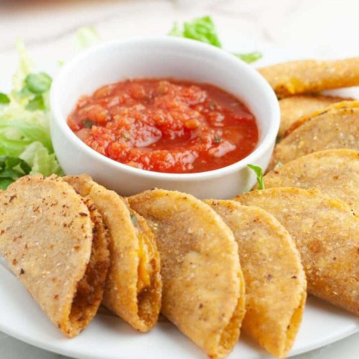 Mini tacos served on a white plate with a side of salsa and green vegetable.