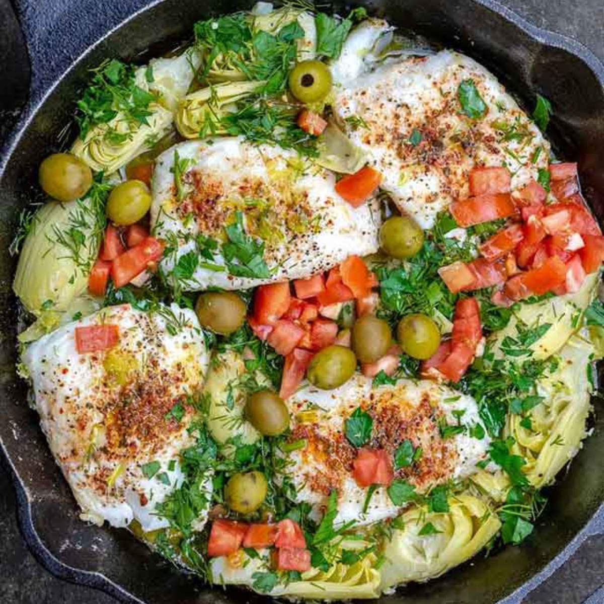 baked cod with artichoke hearts, tomatoes, olives, and herbs served on skillet