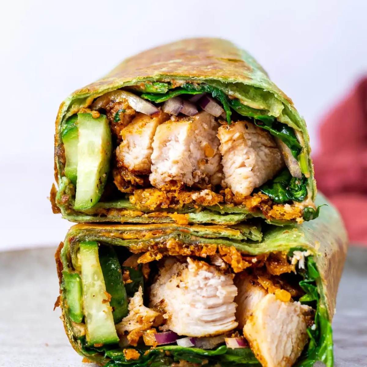 A photo of a Chicken Wrap cut in half, showing shredded chicken, cucumber, red onion, and a sauce inside a spinach tortilla.