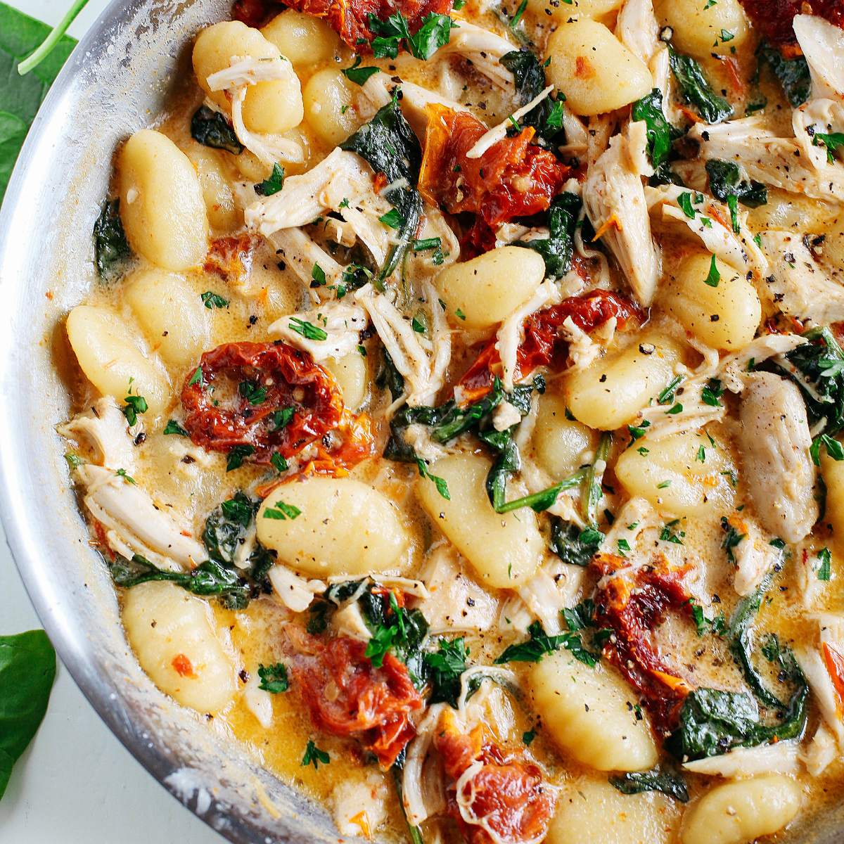 A pan of gnocchi tossed in a creamy sauce with chicken, spinach, and sun-dried tomatoes.