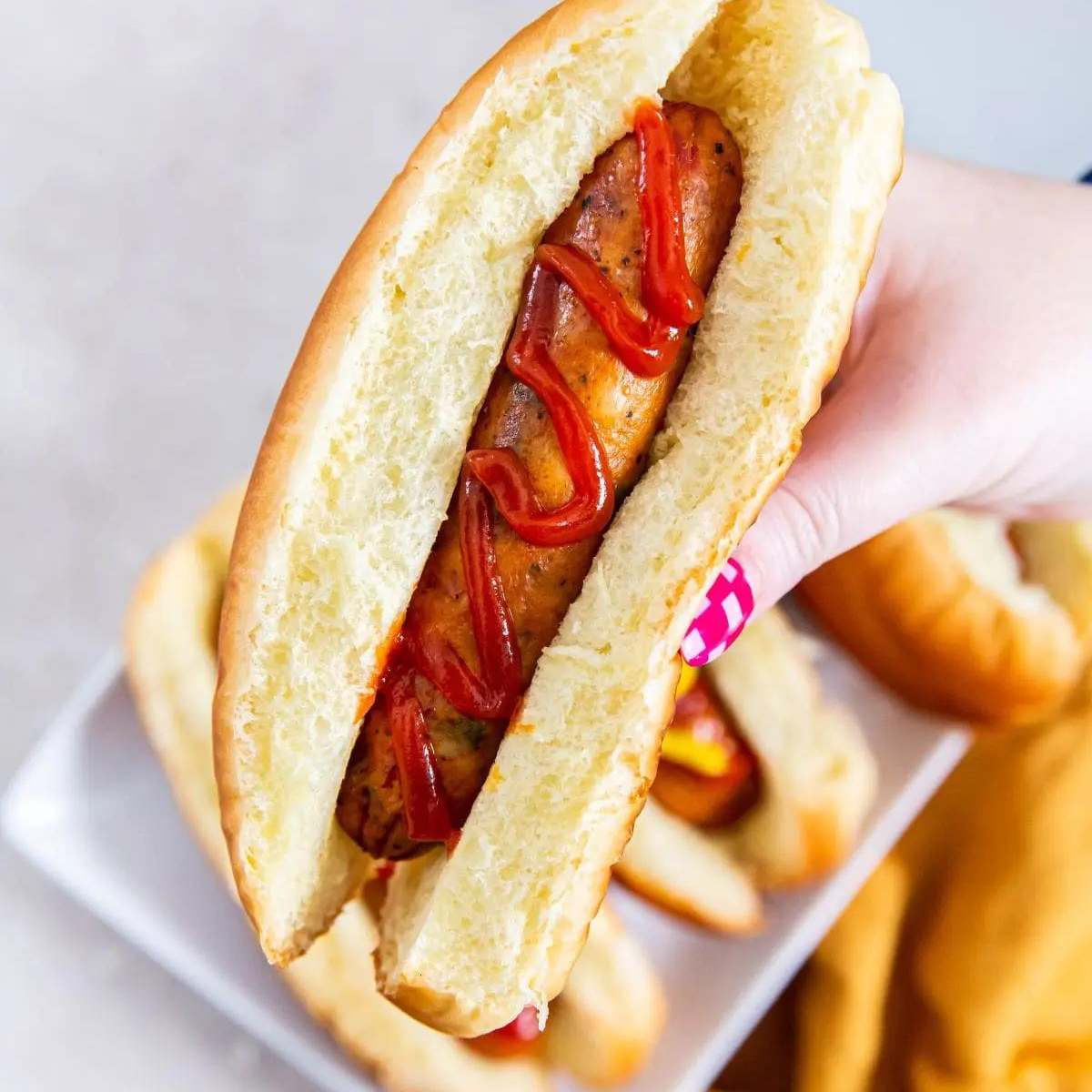 A hand holding a hot dog bun with a grilled chicken sausage and ketchup on top.