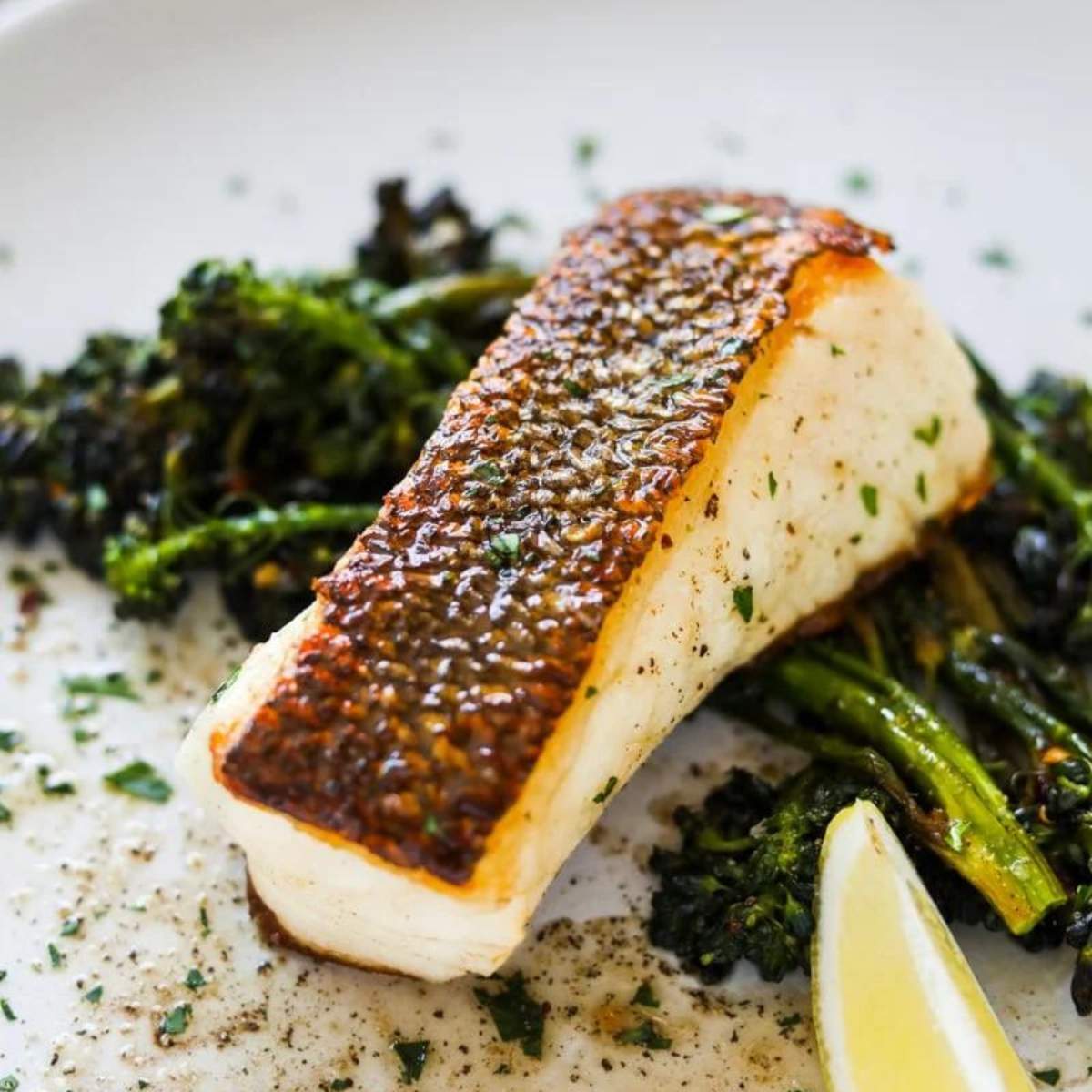 Pan-seared white fish with roasted broccoli and a lemon wedge.