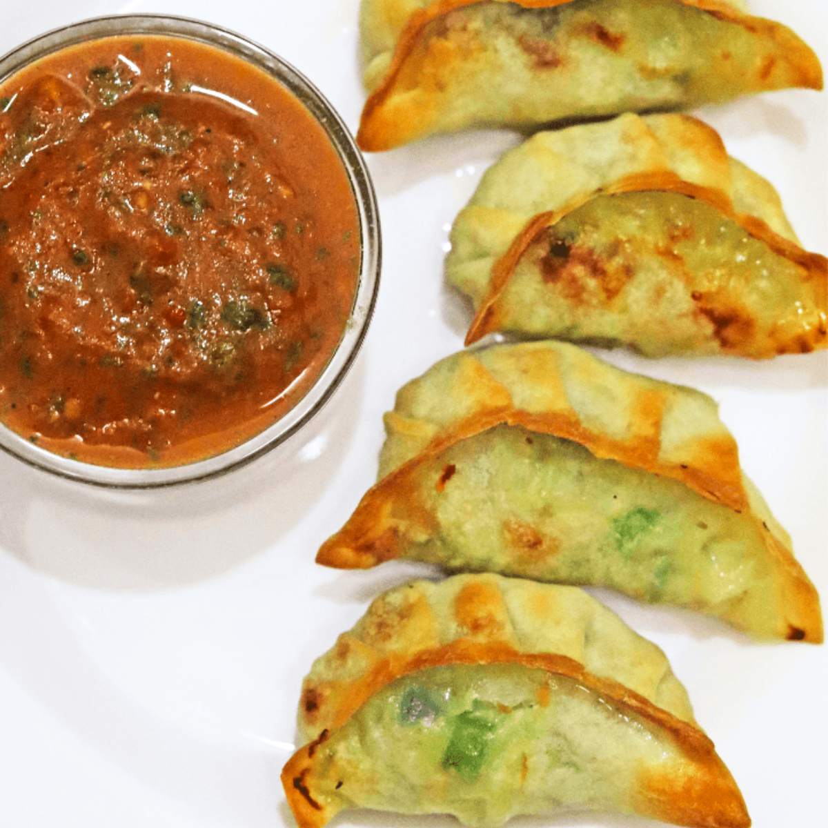  Several golden-brown chicken dumplings served on a plate with a small bowl of dipping sauce.