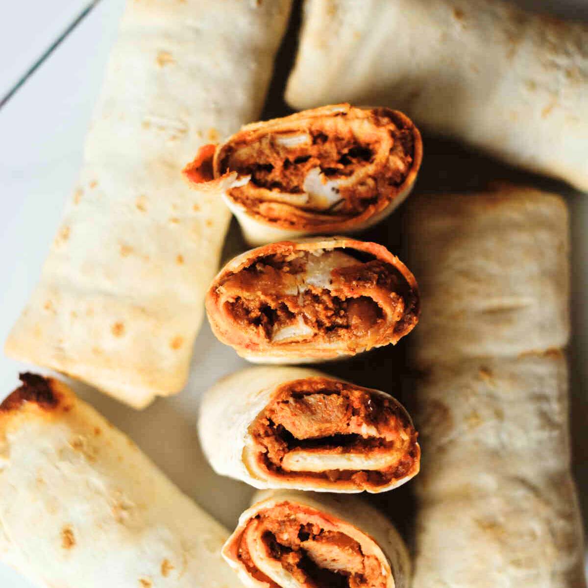 Several crispy, golden-brown burritos cut in half to reveal the filling inside.








