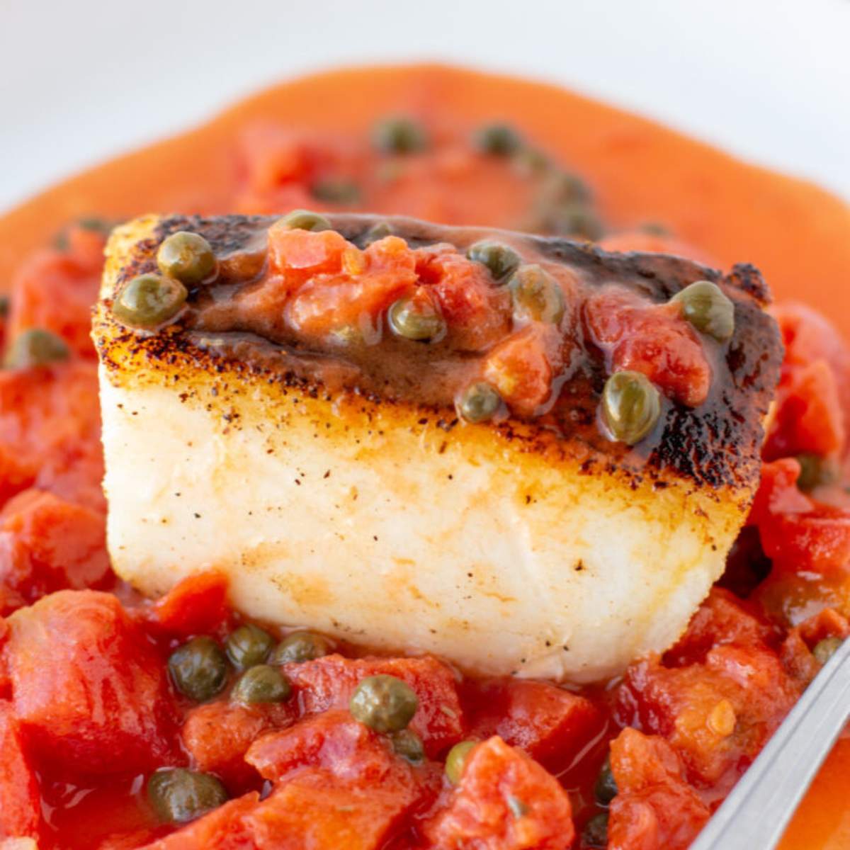 Seared white fish with a tomato, caper, and red butter sauce.