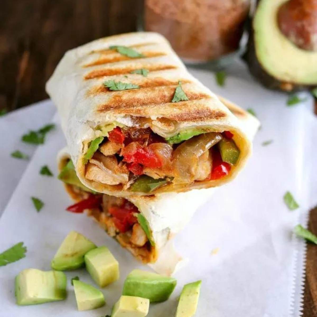 A photo of a grilled chicken fajita wrap cut in half, showing grilled chicken, peppers, onions, and avocado inside a grilled tortilla.