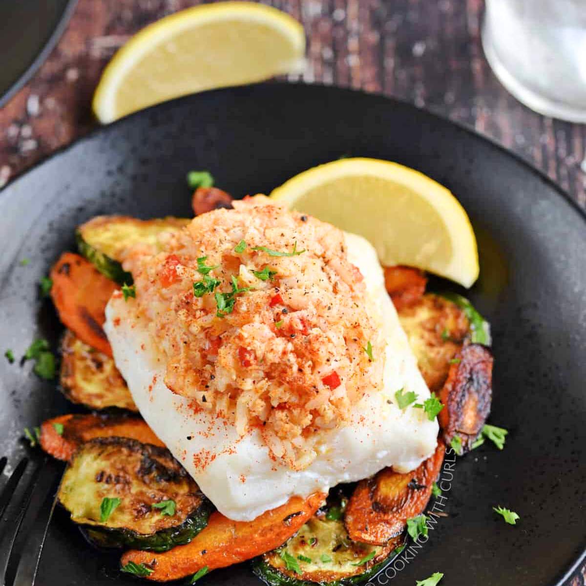 Baked stuffed white fish with a crab and shrimp stuffing served with roasted vegetables, on a black plate.