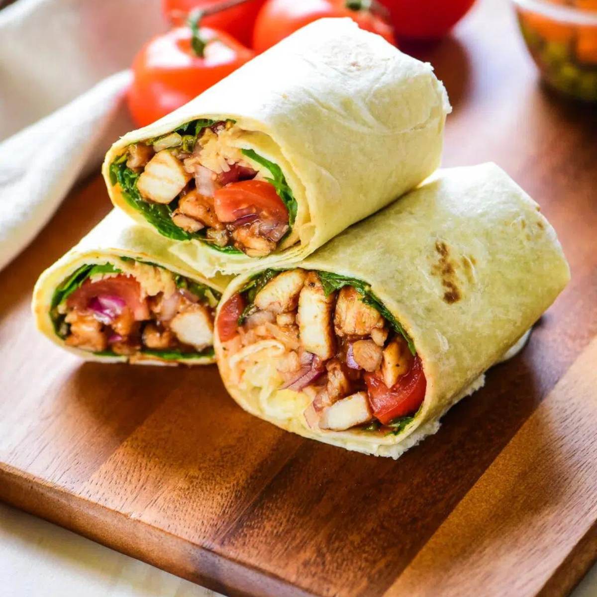 Three Chicken Wraps cut in half, showing shredded BBQ chicken, lettuce, tomato, red onion, and a creamy sauce inside tortillas.