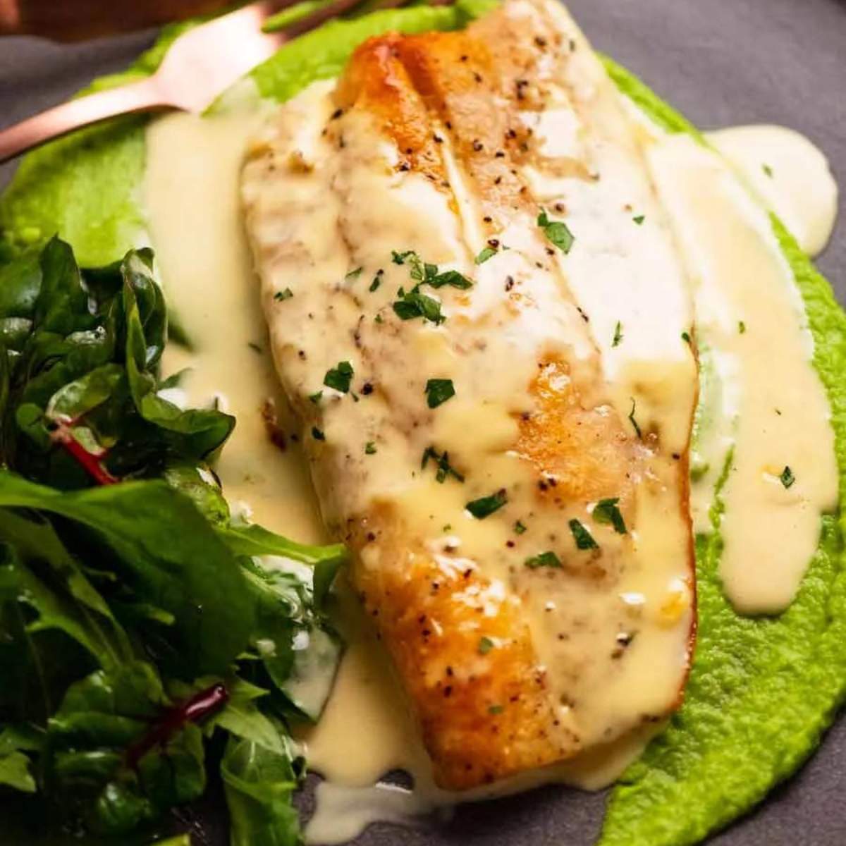 Pan-seared fish with a creamy white wine sauce, served over a bed of mashed peas and accompanied by a side salad.

