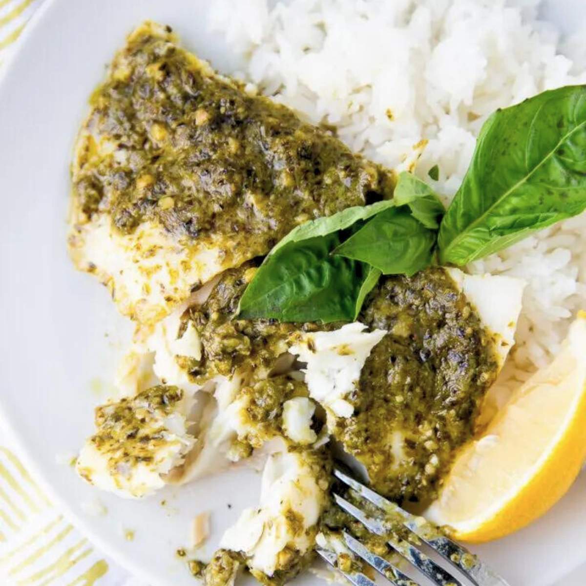 white fish with pesto served over rice and garnished with fresh basil.