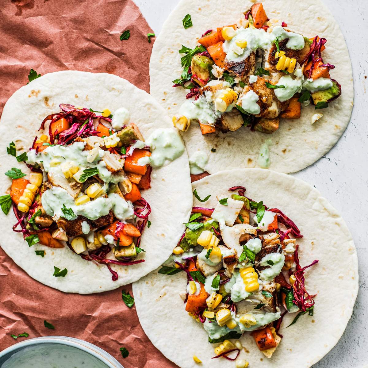 Three fish tacos filled with grilled fish, vegetables, and a creamy green sauce.

