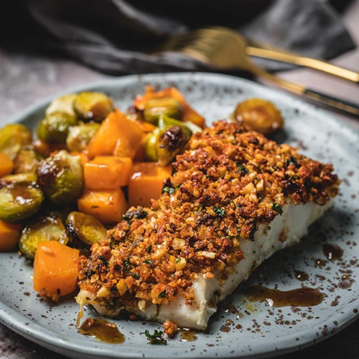 Almond-crusted cod served with roasted crunchy nut crust and and a delicious drizzle of balsamic sauce. There are vegetables on the side.