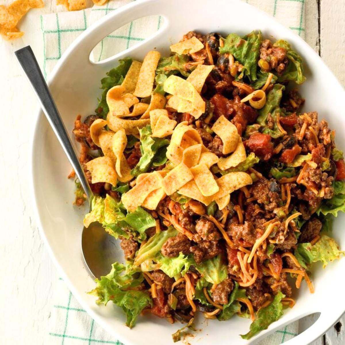  A bowl of ground beef taco salad with lettuce, tomatoes, beans, corn, and tortilla chips.