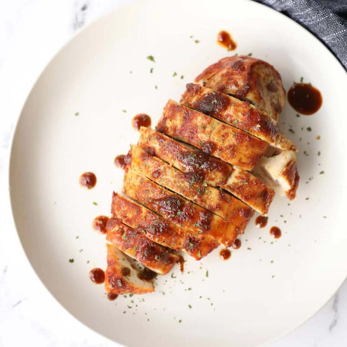 Juicy air fryer chicken breast, sliced and served on a white plate, with a drizzle of sauce.