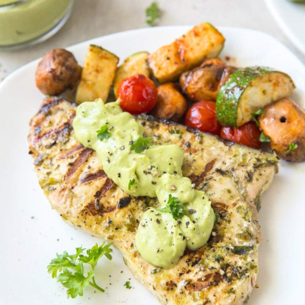 Grilled chicken skewers with cherry tomatoes, bell peppers, and fresh mint served on a white plate.