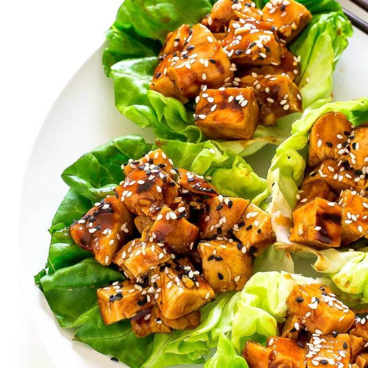 Three lettuce wraps filled with shredded chicken coated in a sweet and savory hoisin sauce, topped with sesame seeds.