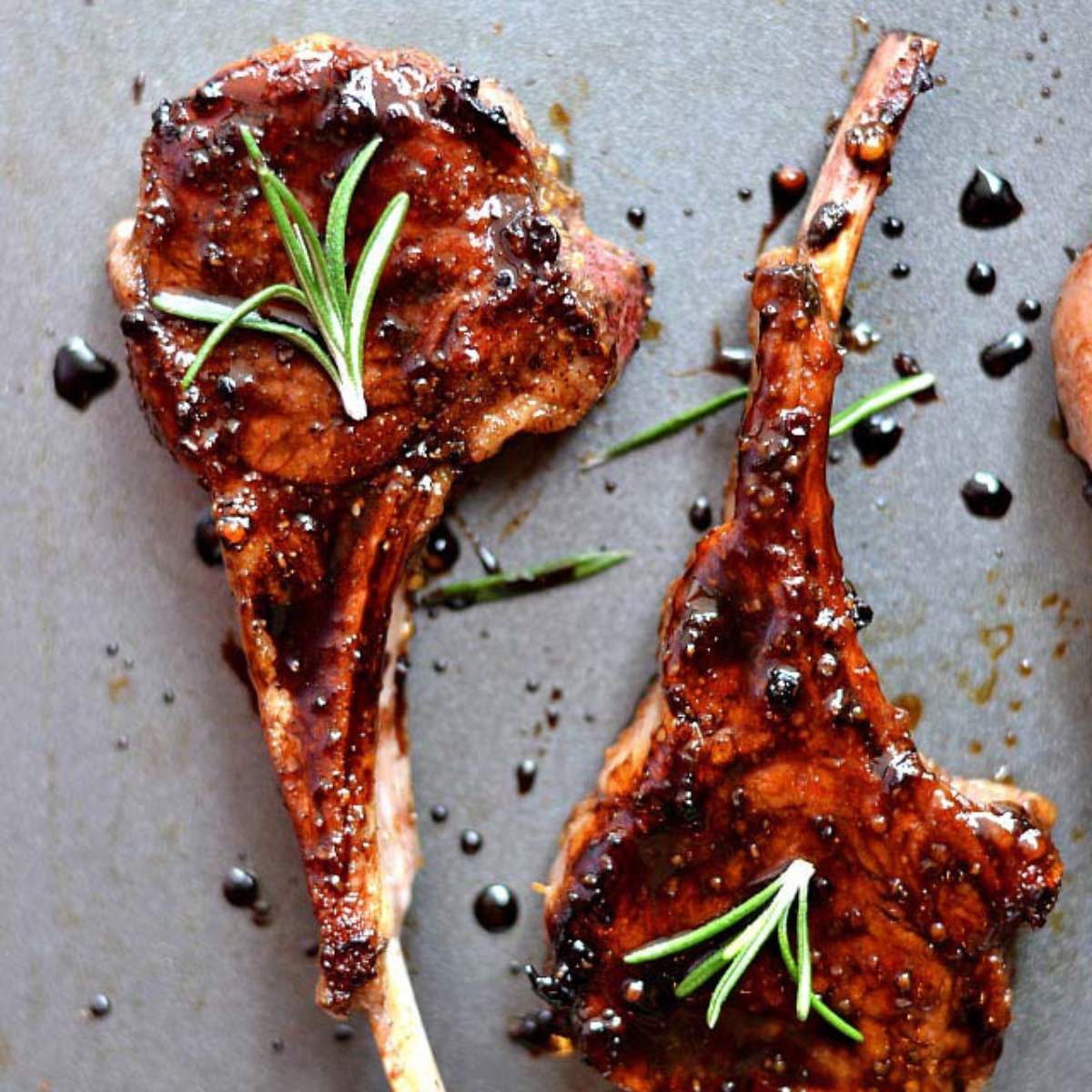 Two lamb chops seasoned with herbs and spices, cooked to a golden brown, and served with rosemary sprigs.