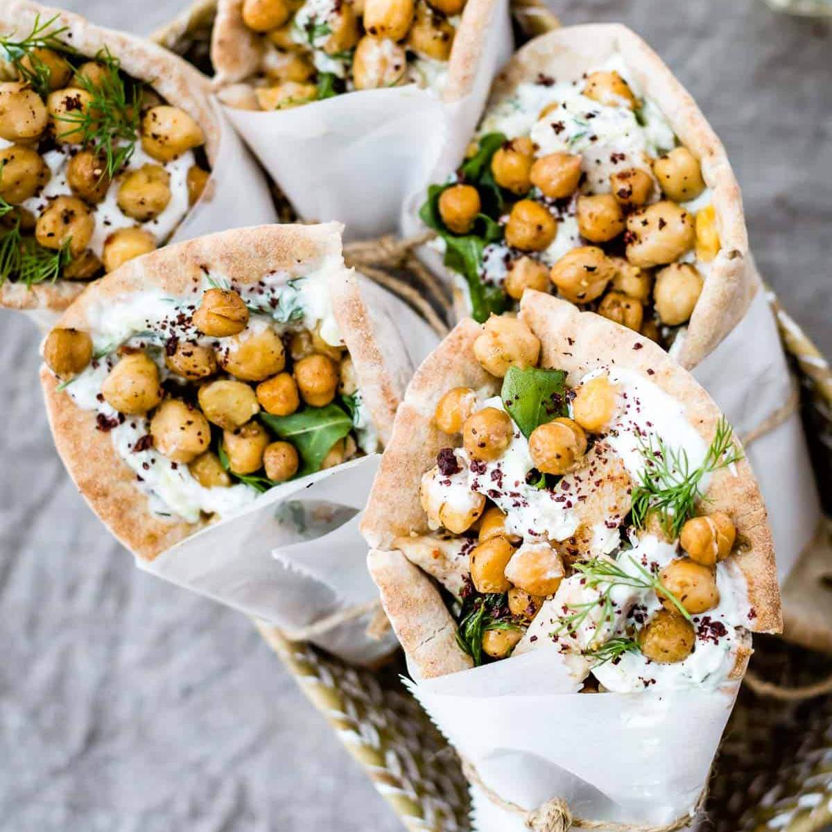 Several shredded chicken wrapped in pitas, showing chickpeas, greens, and a creamy sauce inside the pita bread.