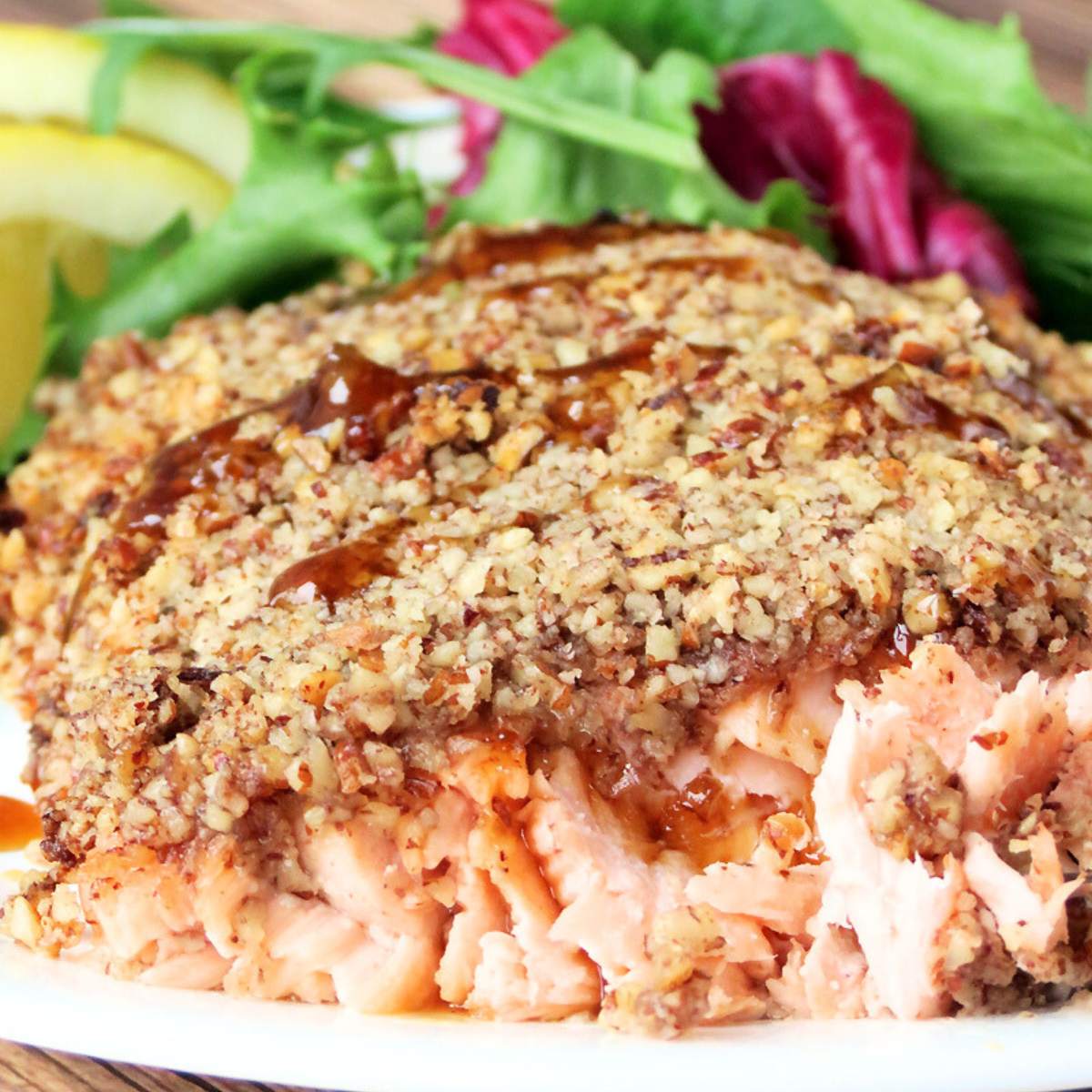 A piece of salmon fillet with a golden-brown pecan crust, served with a side salad. The salmon is flaky and cooked through.