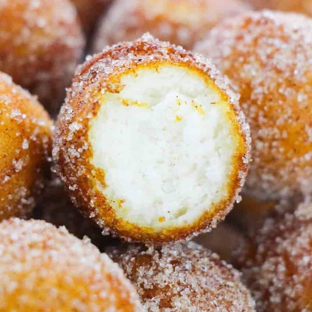 A close-up of a cinnamon sugar donut hole with a bite taken out of it, showing the fluffy interior.