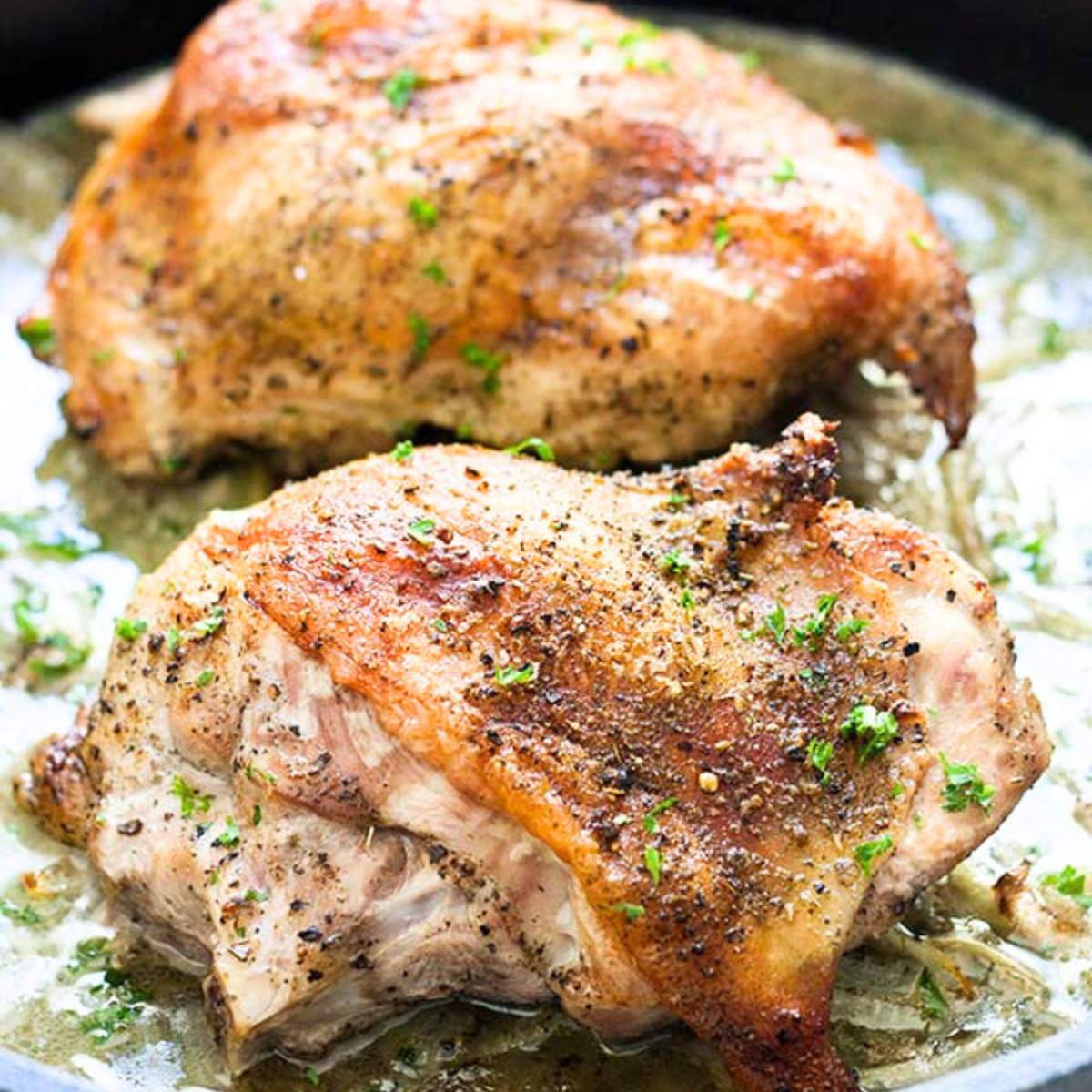 Two roasted turkey thighs in a pan, seasoned with herbs and spices.