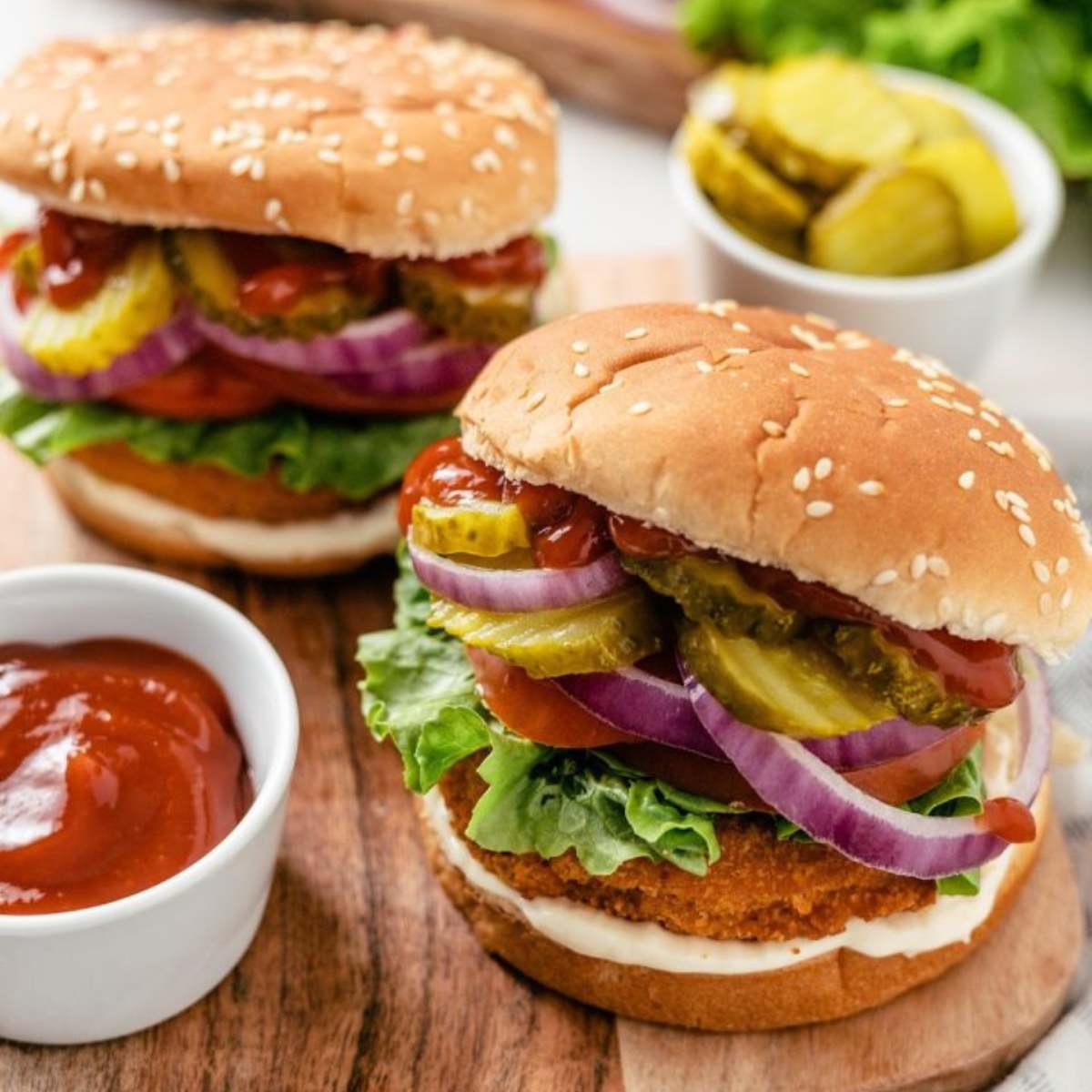  Two crispy chicken burgers on sesame seed buns, topped with lettuce, tomato, onion, pickles, and ketchup.