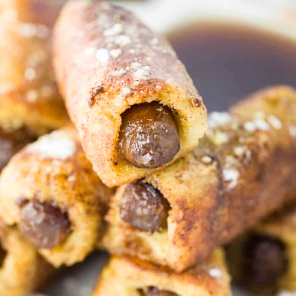 A stack of crispy French toast roll-ups, each filled with savory sausage and coated in a sweet cinnamon-sugar mixture.

