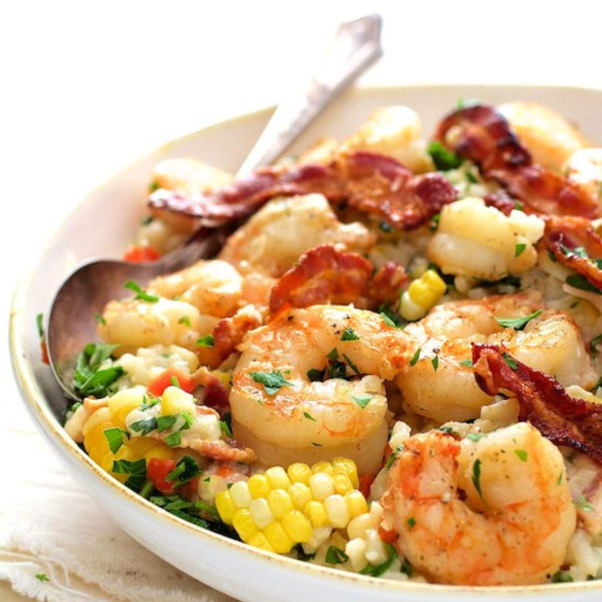 A bowl of creamy risotto with cooked shrimp, corn kernels, and crispy bacon.