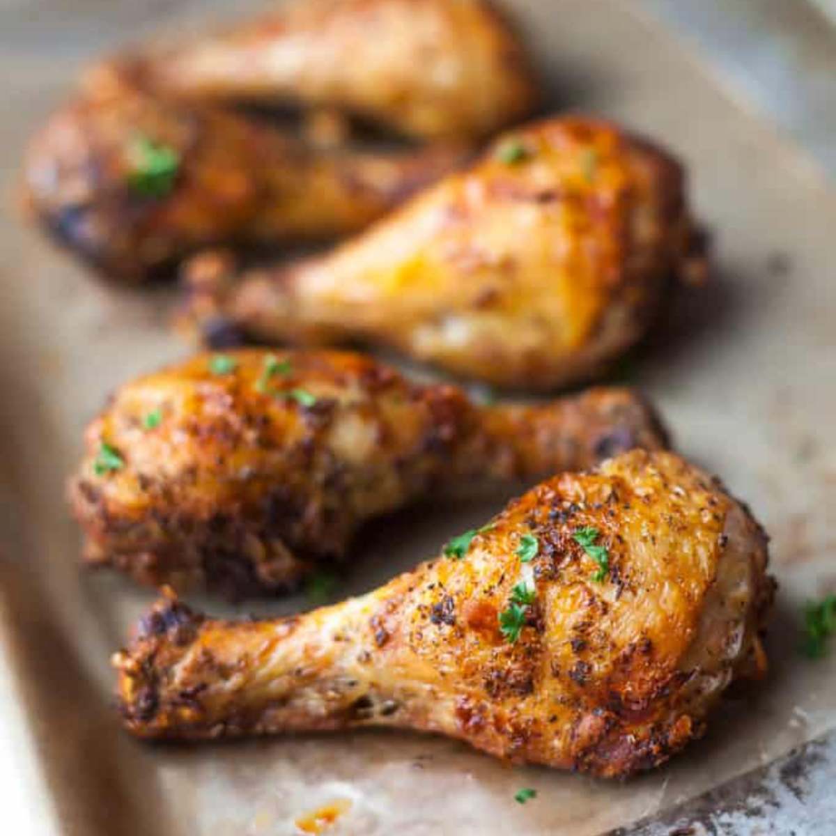 Crispy, golden-brown chicken drumsticks seasoned with herbs and spices, served on a baking sheet.