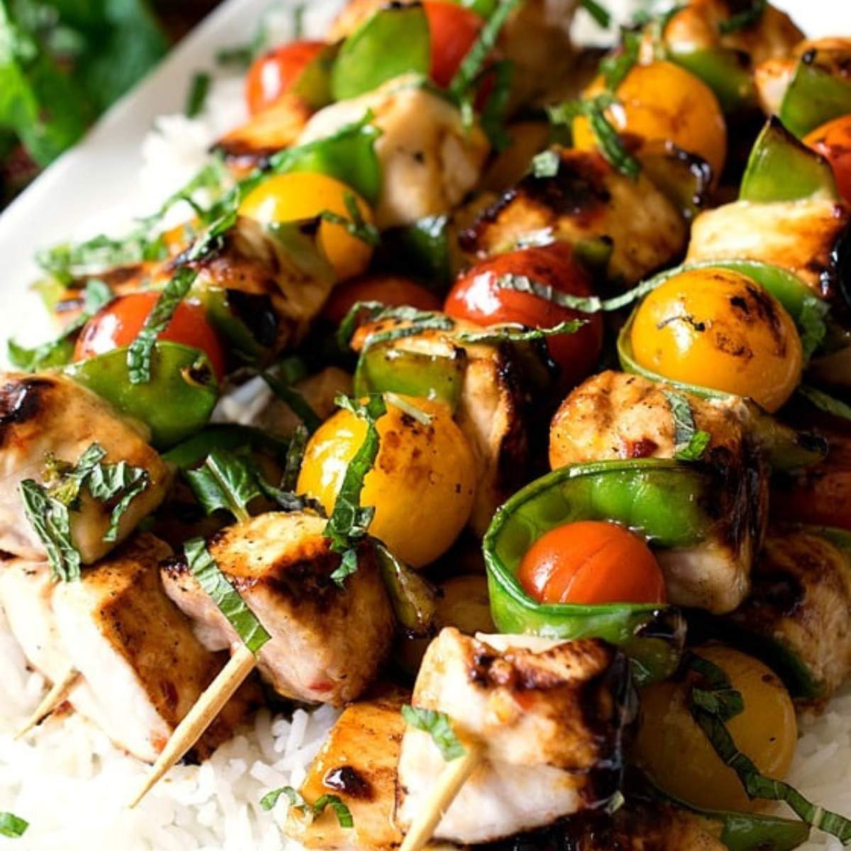 Grilled white fish skewers with cherry tomatoes, bell peppers, and fresh mint served over rice.