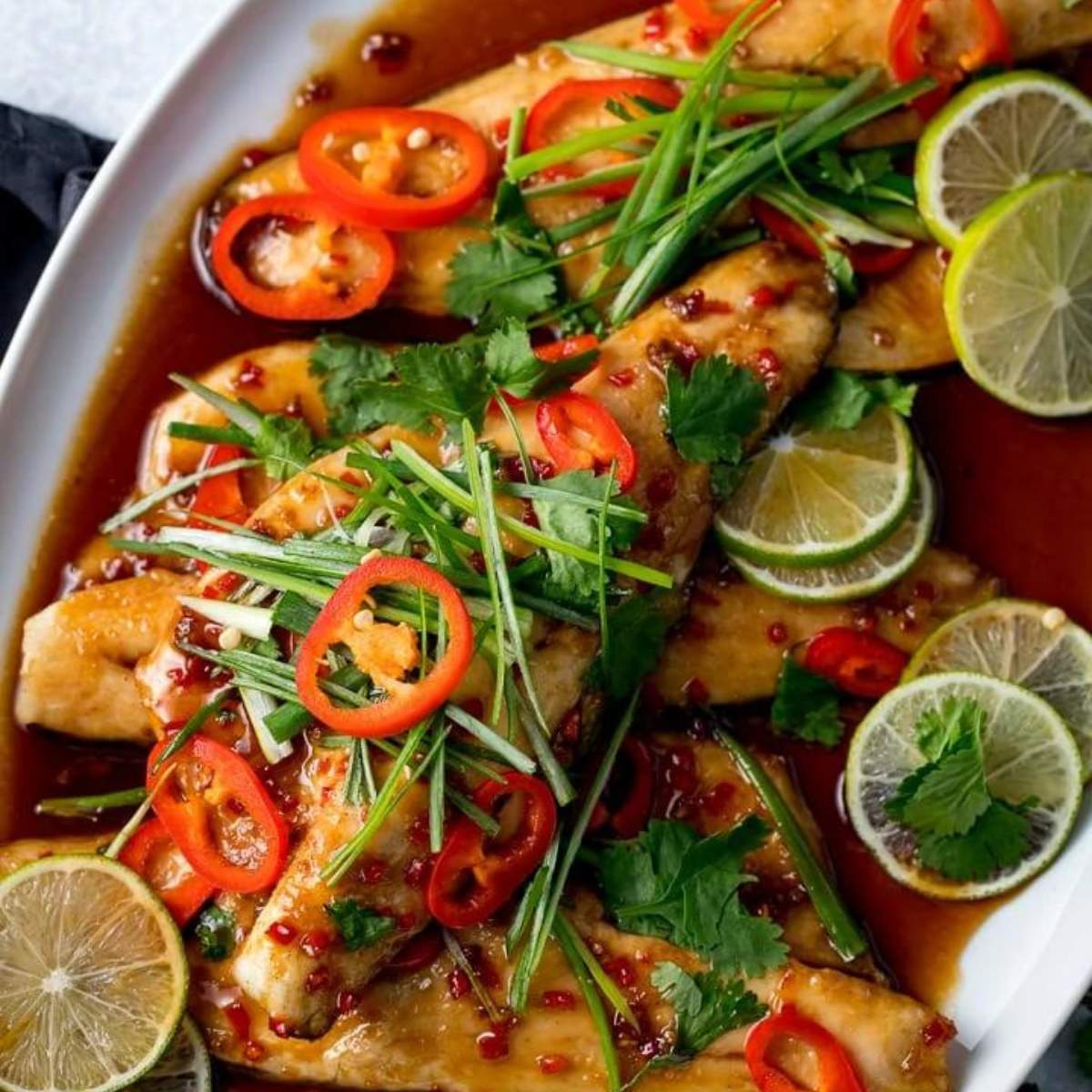 Pan-seared fish fillets with a sweet and spicy chili sauce, topped with fresh cilantro, green onions, and red chili peppers.