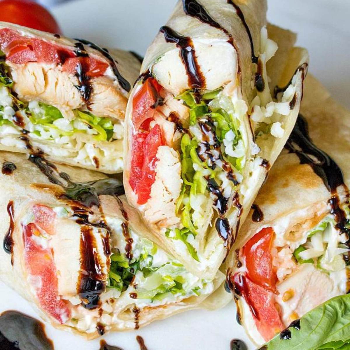 Several Chicken Wraps cut in half, showing grilled chicken, tomatoes, mozzarella cheese, and black sauce glaze inside tortillas.