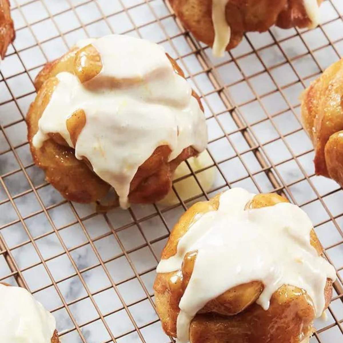 A batch of gooey cinnamon rolls, freshly baked and topped with a sweet glaze, cooling on a wire rack.