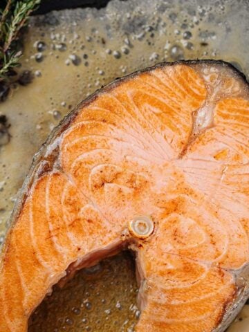 frying salmon steak on parchment paper with butter and rosemary