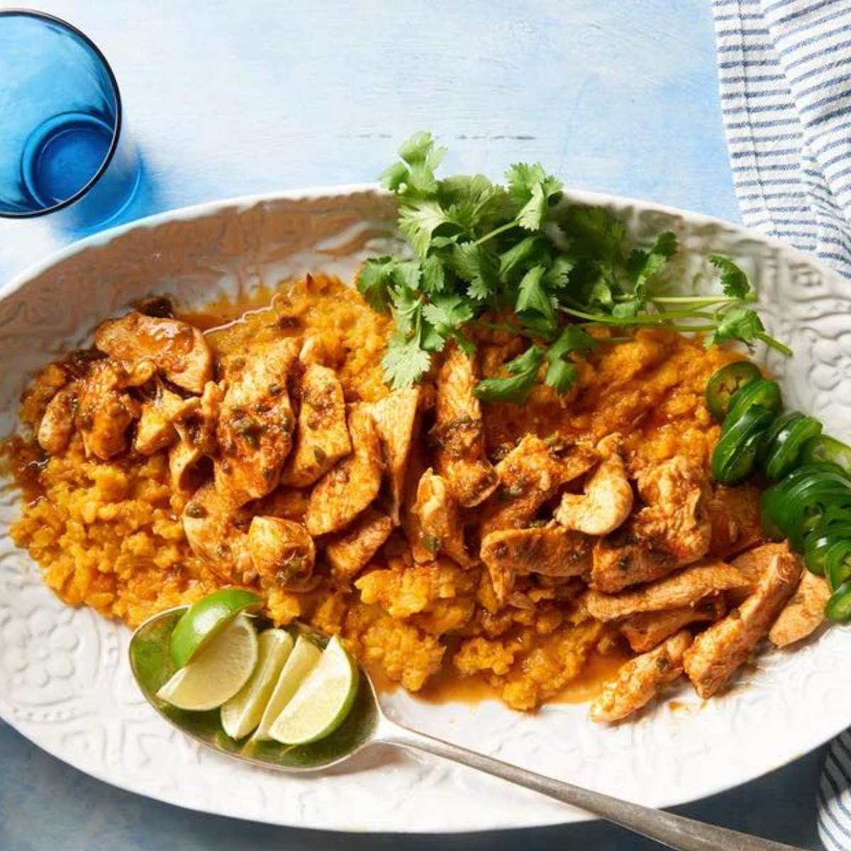 A platter of sliced chicken served over a bed of mashed butternut squash. The chicken is seasoned with a spicy chili sauce and garnished with fresh cilantro and lime wedges.