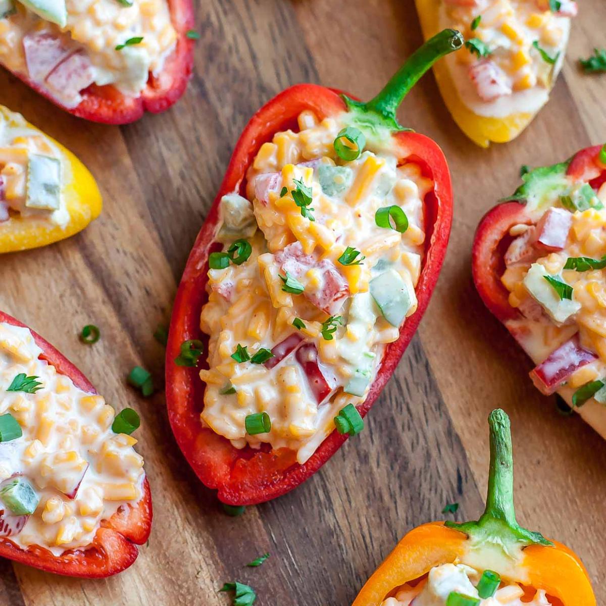 Stuffed mini peppers with a creamy cheese mixture, topped with chopped green onions and parsley. Served on a wooden board.