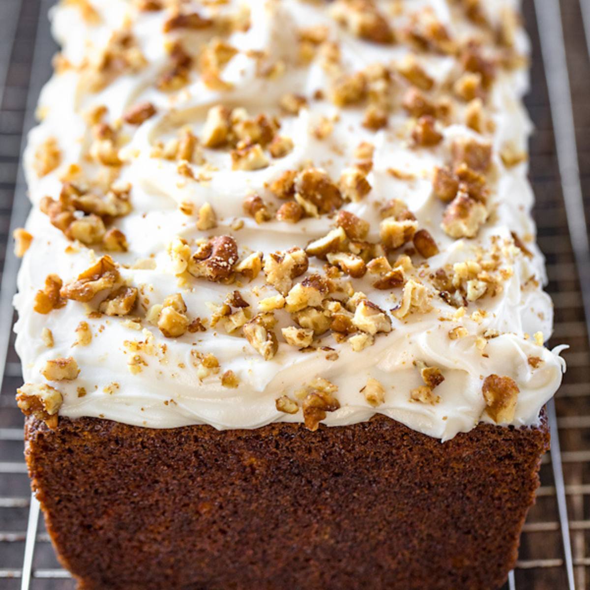 A loaf of carrot cake topped with cream cheese frosting and chopped pecans.