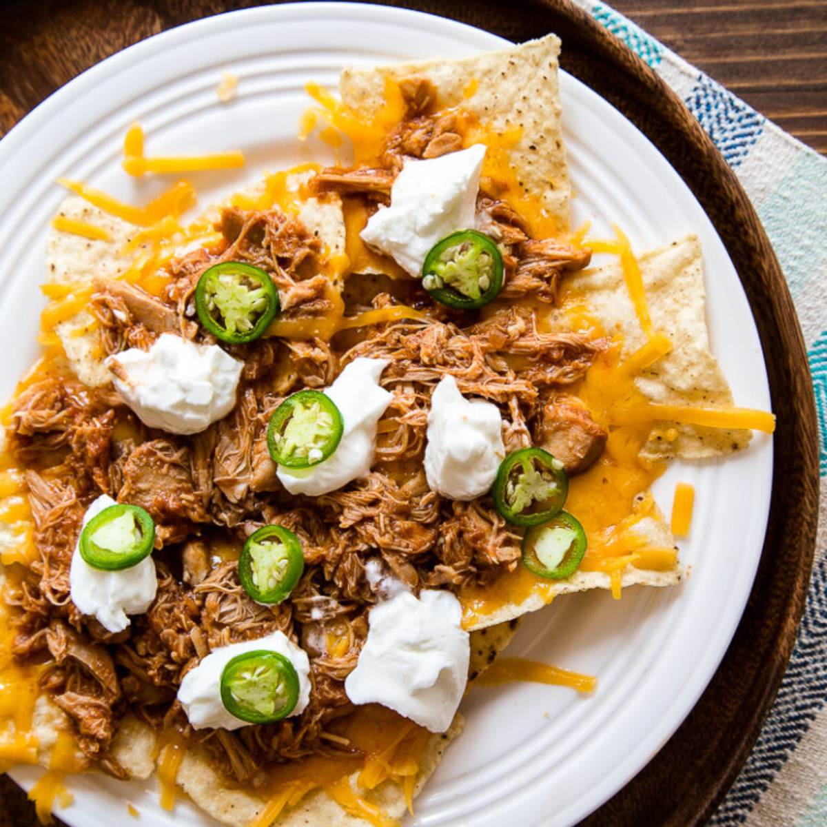 A plate of nachos topped with shredded chicken, melted cheese, sour cream, and sliced jalapeño peppers.