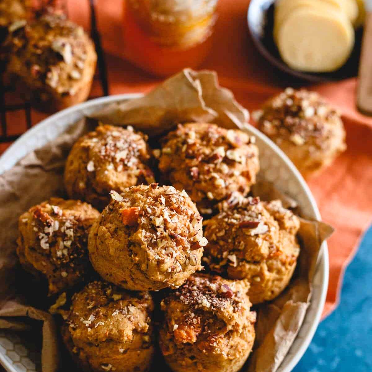 A bowl of mini pumpkin muffins with chopped pecans on top, served with butter and honey on the side.