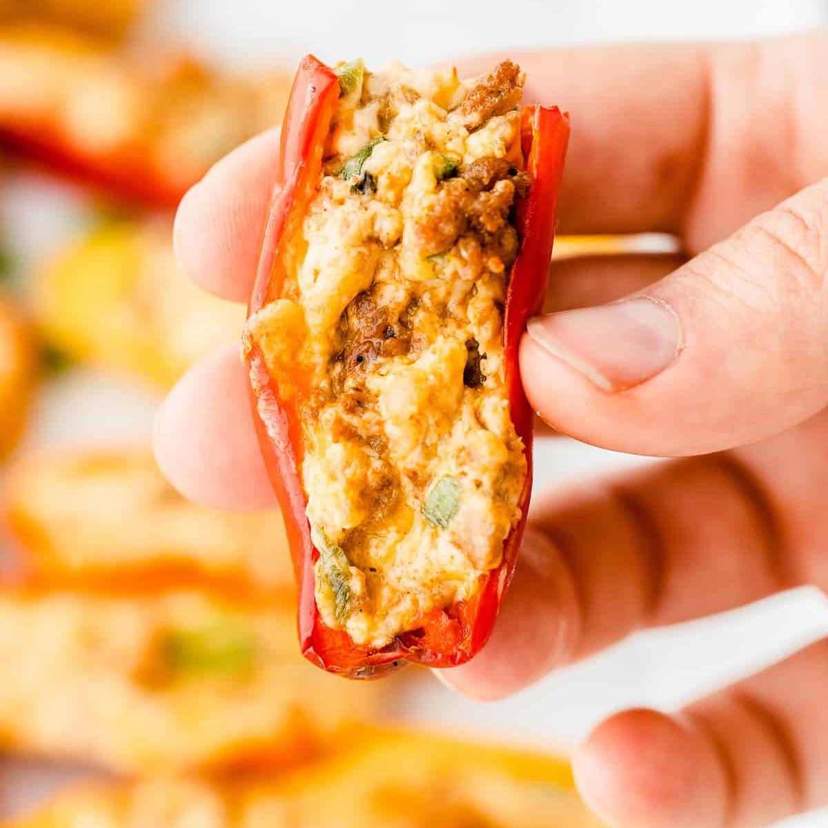  A close-up of a hand holding a stuffed mini pepper, showing the creamy filling and a hint of green onion.