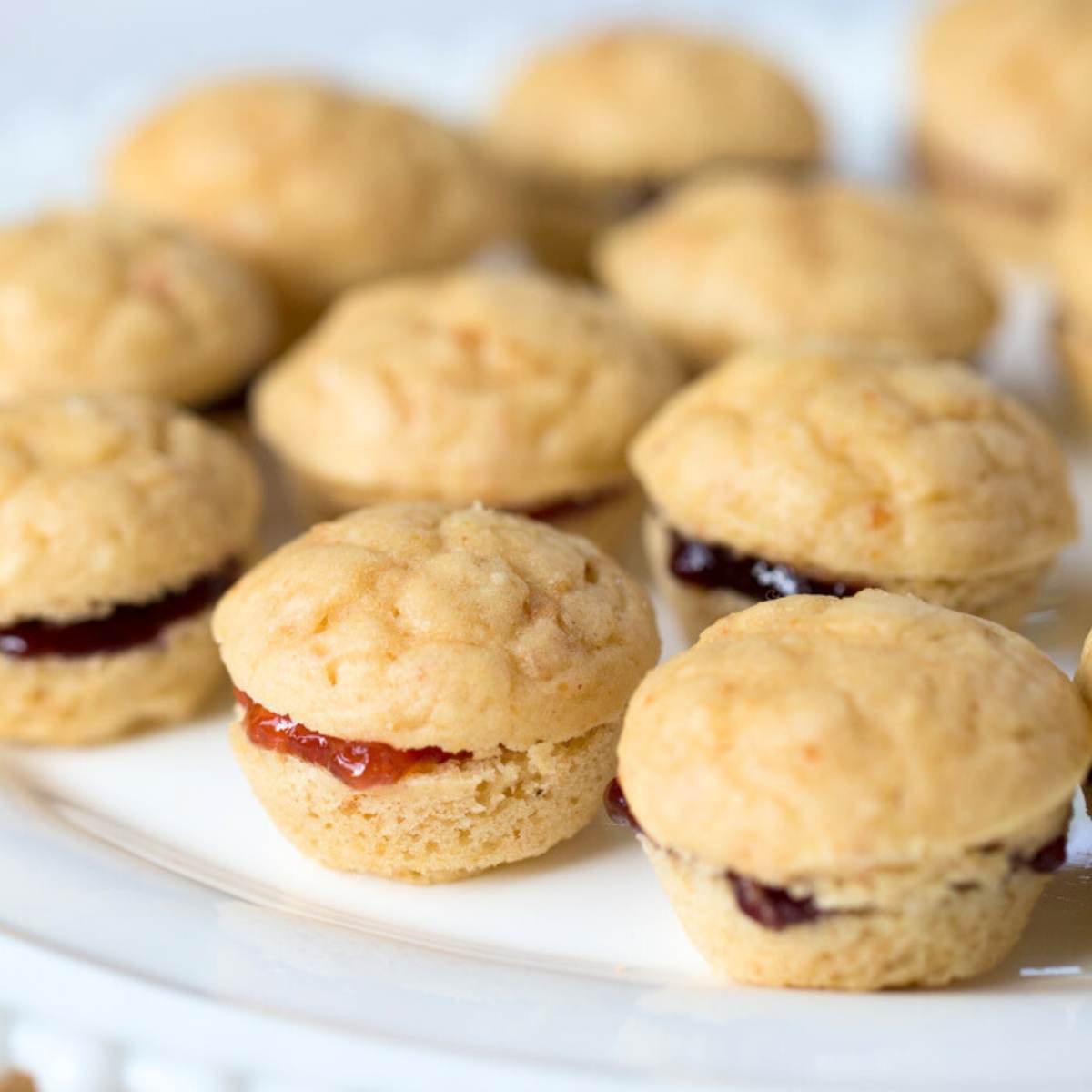 A plate of mini peanut butter and jelly muffins, with the jelly filling visible in the center of each muffin.