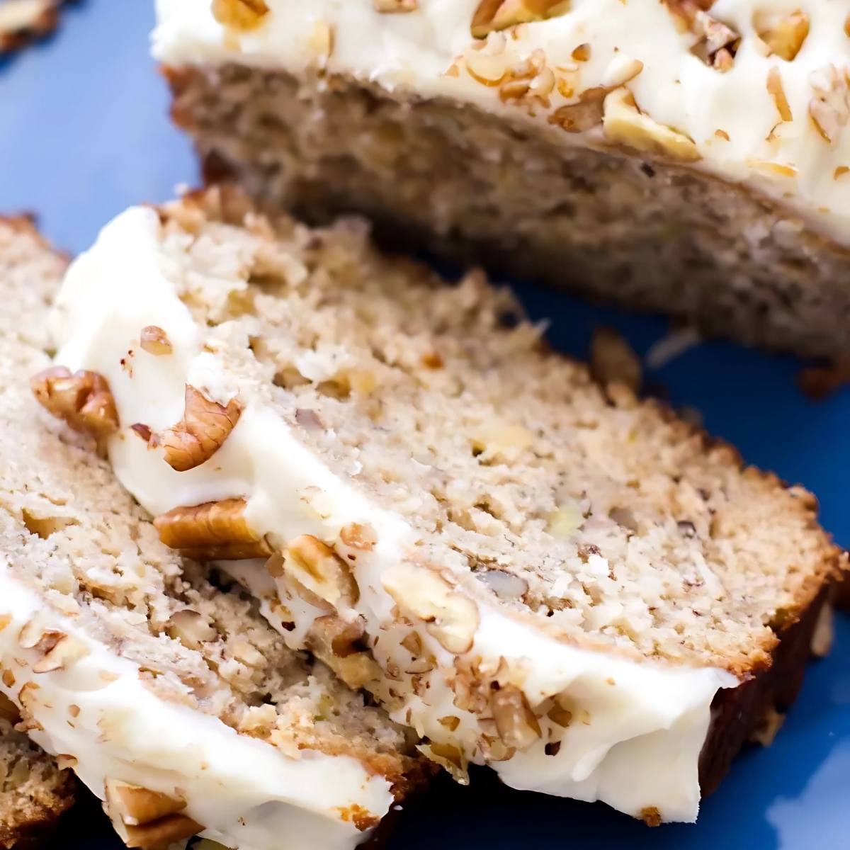 A close-up of slices of banana bread with cream cheese frosting and chopped pecans.