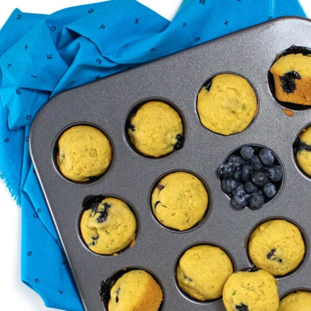  A muffin tin filled with baked blueberry muffins, with a pile of blueberries next to it.