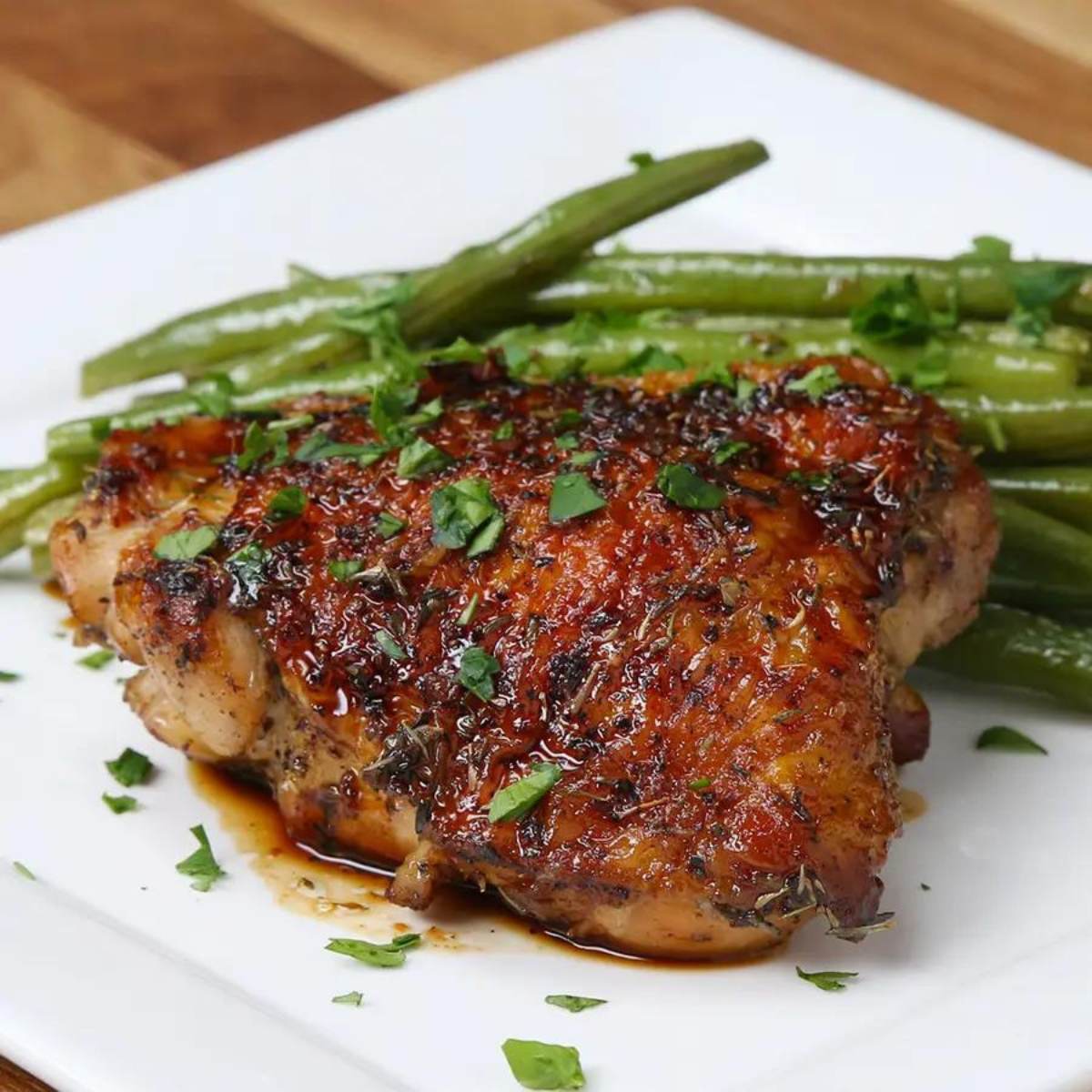 A plate of honey garlic chicken with a side of green beans. The chicken is glazed with a sweet and savory sauce and garnished with fresh parsley.