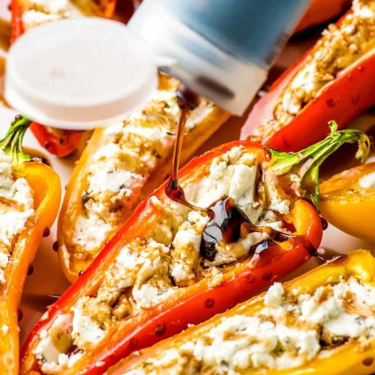 Baked mini peppers filled with a creamy cheese mixture, with balsamic glaze being drizzled over them.