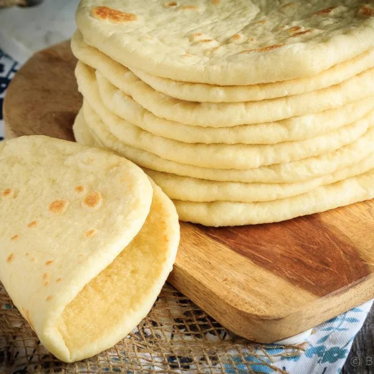 A stack of golden-brown flatbreads on a wooden cutting board, with one flatbread partially folded open.