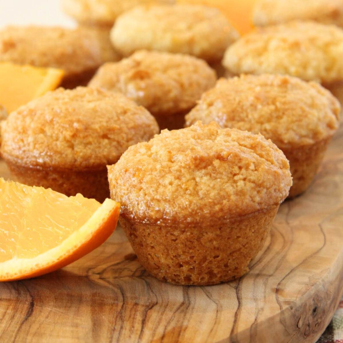 A group of orange muffins on a wooden cutting board, with a slice of orange next to them.